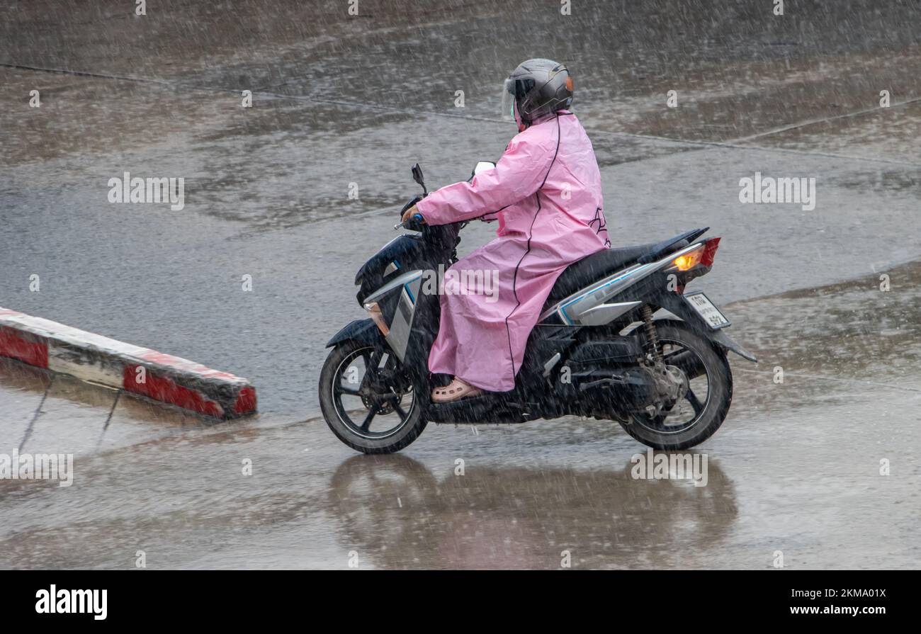 Ein Motorradfahrer mit Regenjacke fährt bei starkem Regen auf einer nassen Straße Stockfoto