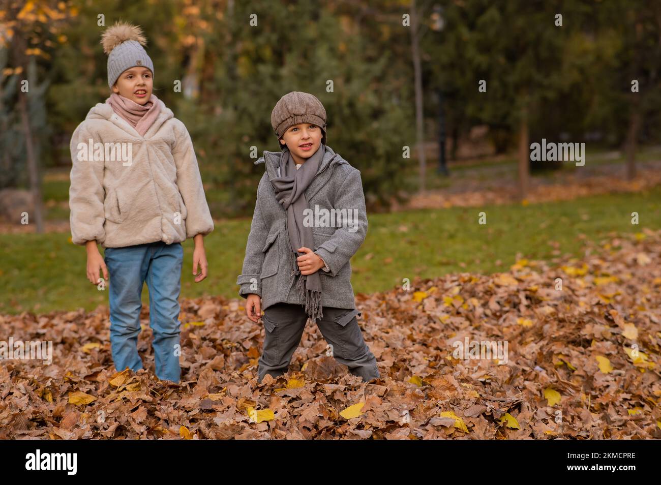 Kaukasische Kinder gehen im Herbstpark spazieren. Bruder und Schwester in Mänteln. Stockfoto