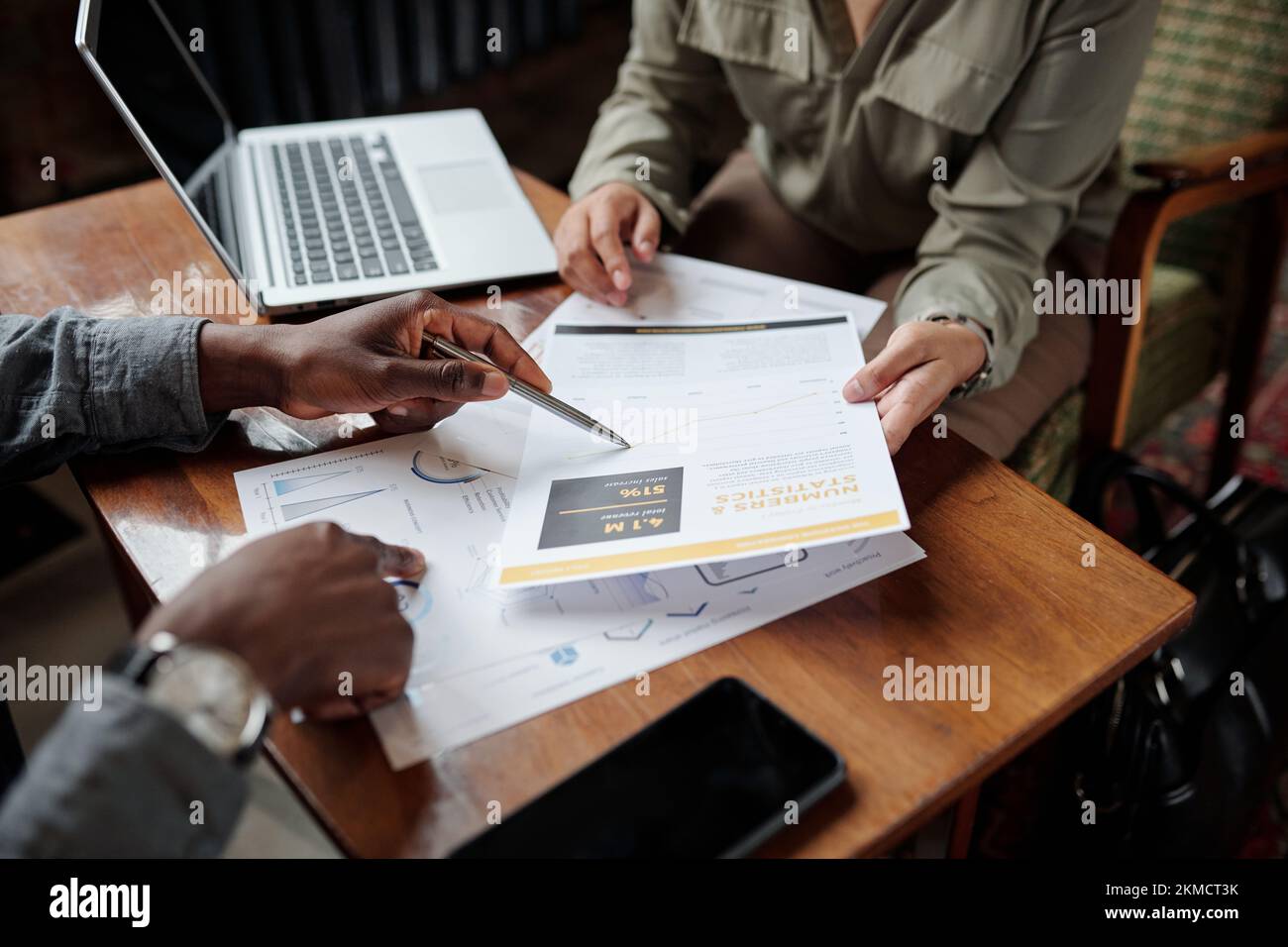 Hand eines jungen schwarzen Mannes mit Stift, der auf ein Finanzdokument zeigt, während er der Kollegin während des Gesprächs Daten erklärt Stockfoto