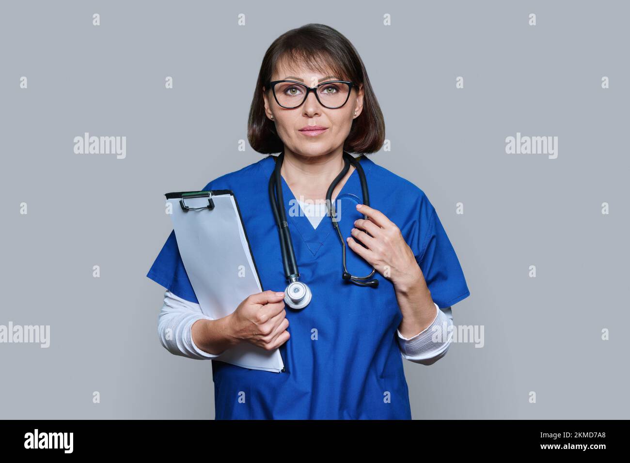 Porträt einer Ärztin mit Clipboard, das auf grauen Hintergrund in die Kamera schaut Stockfoto