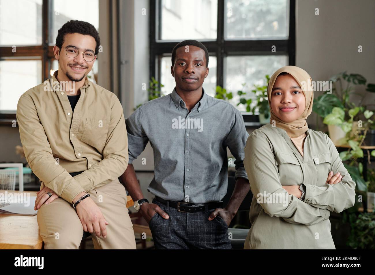 Eine Gruppe von drei jungen multikulturellen Mitarbeitern in Freizeitkleidung, die in einem Büro im Freiraum vor der Kamera stehen und Sie ansehen Stockfoto