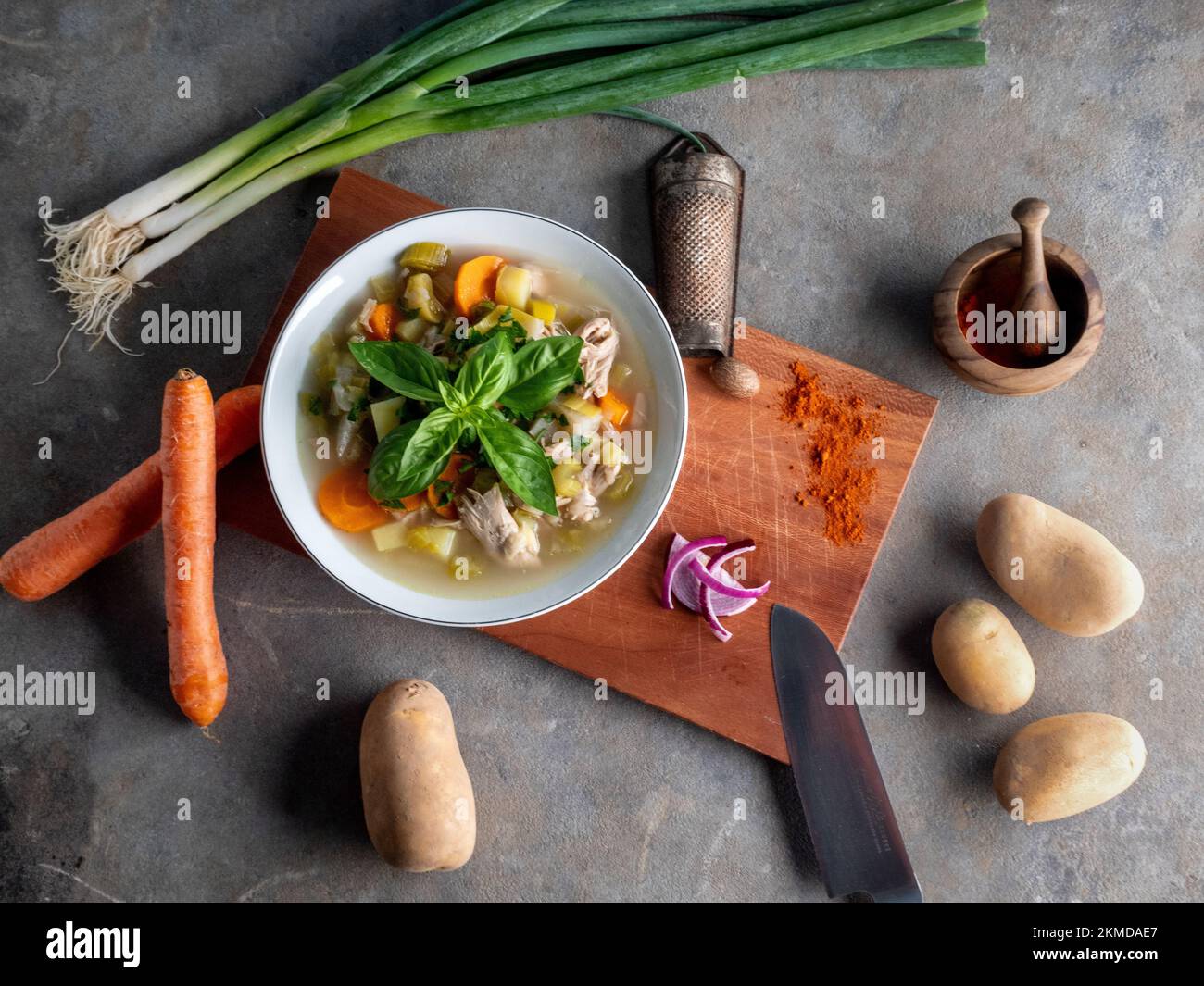 Ein Blick von oben auf eine Schüssel Suppe auf dem Holzbrett, umgeben von Gemüse und notwendigen Gegenständen Stockfoto