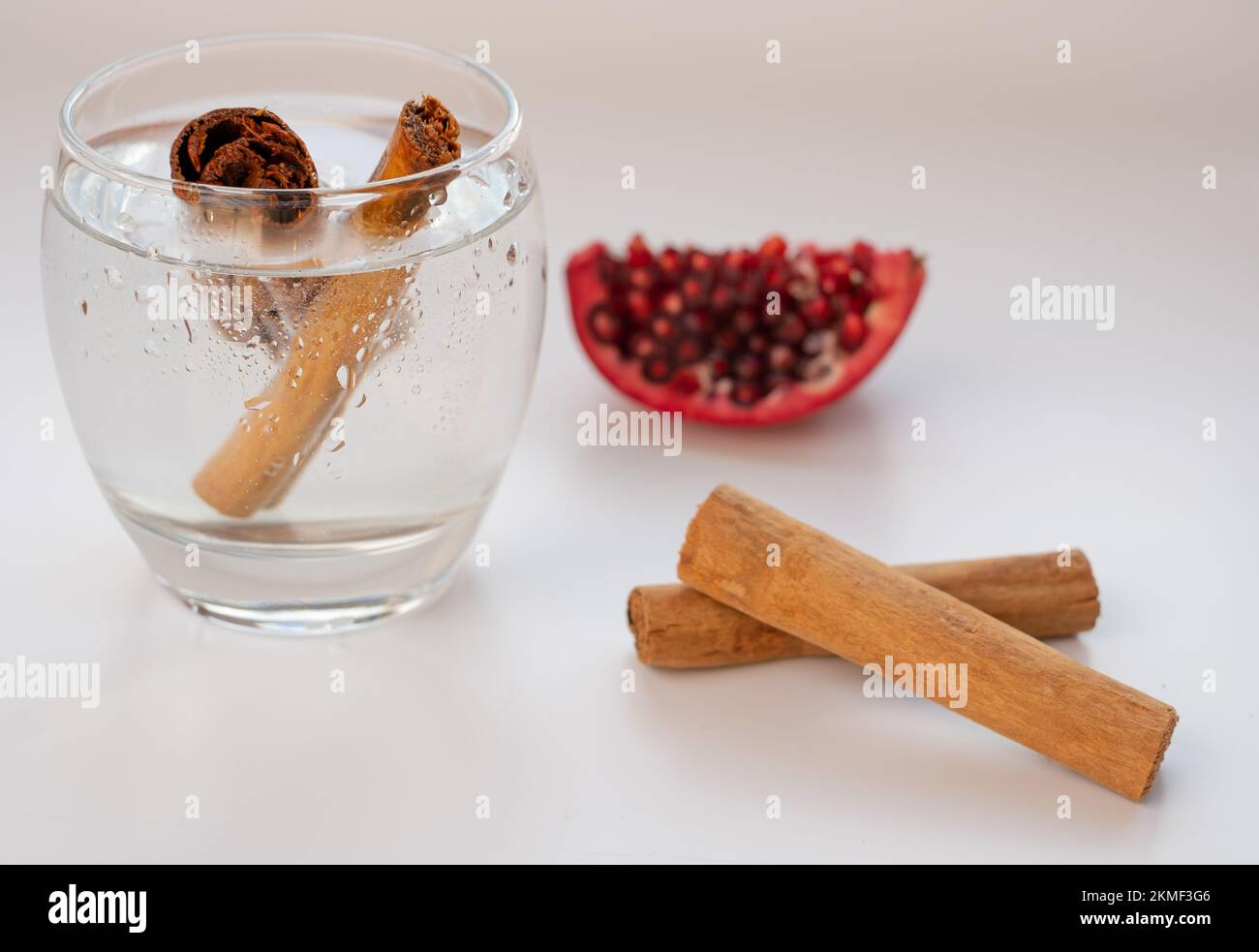 Zimt in einem Glas Wasser. Zimtbecher und Granatapfel auf weißem Hintergrund. Stockfoto