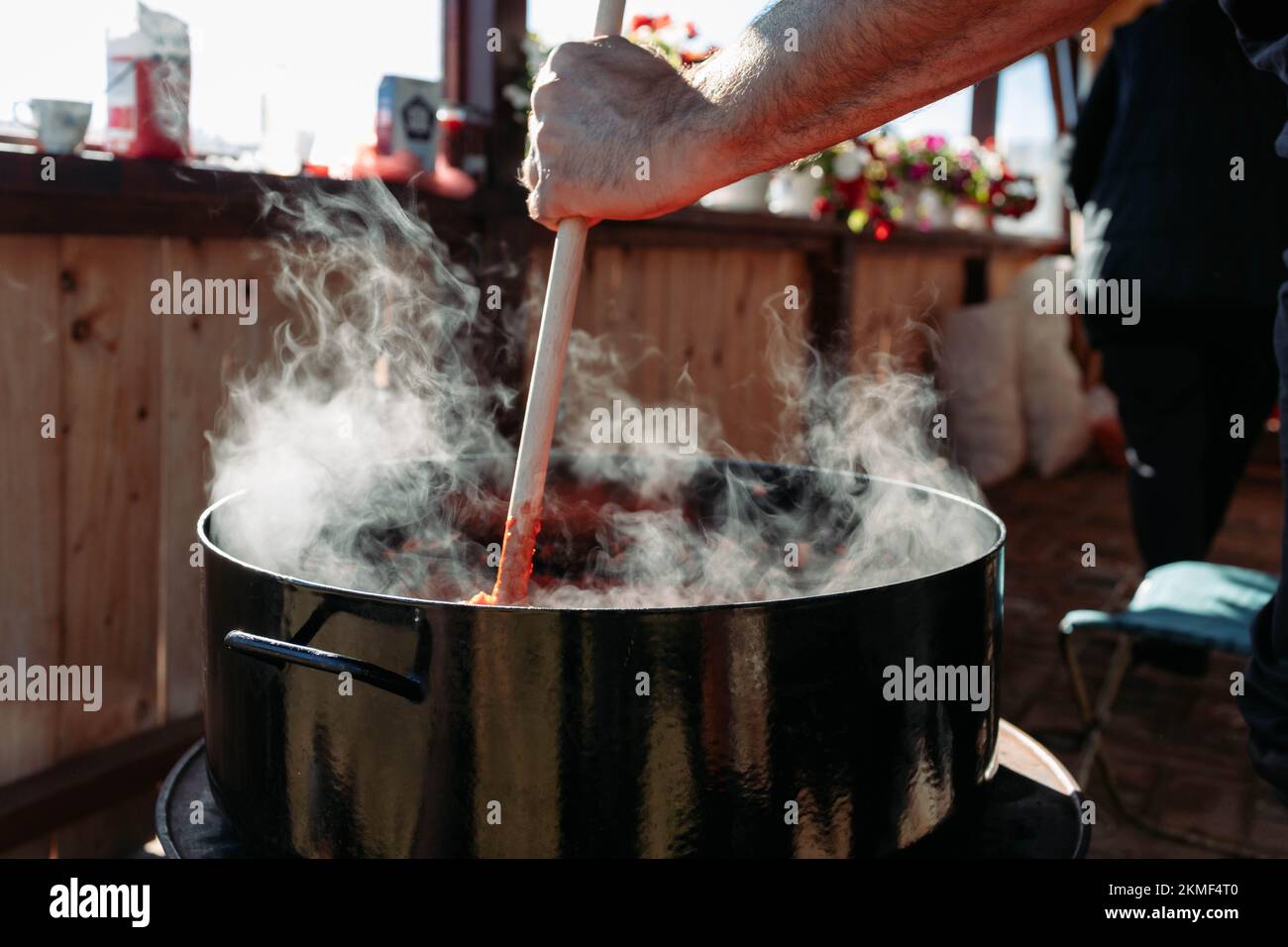 Männliche Hand rührt Ajvar in einem großen Topf. Ajvar, traditionelle Zubereitung von Mahlzeiten Stockfoto