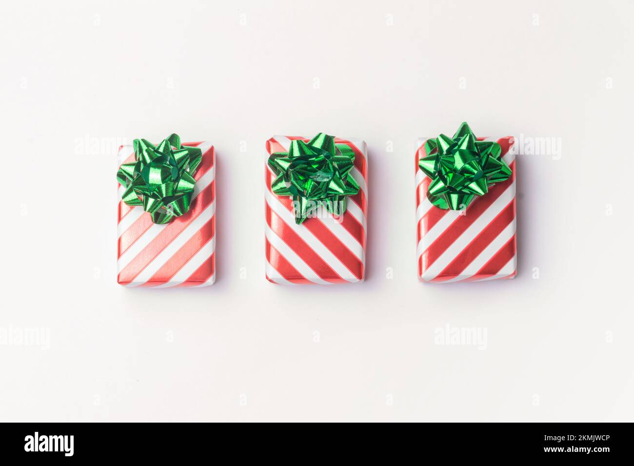 Weihnachtsgeschenke und Silvestergeschenke in rot gestreiftem Geschenkpapier mit grünen Schleifen auf weißem Hintergrund und Kopierbereich. Stockfoto