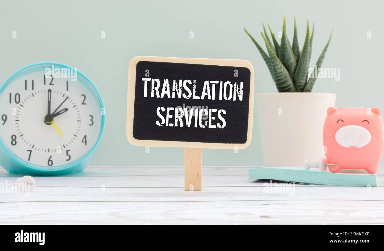Auf einem Holztisch befinden sich Berichte, eine Topfpflanze, eine Lupe, ein schwarzer Stift und ein Notizbuch mit den ÜBERSETZUNGSDIENSTEN. Geschäftsbetrieb Stockfoto