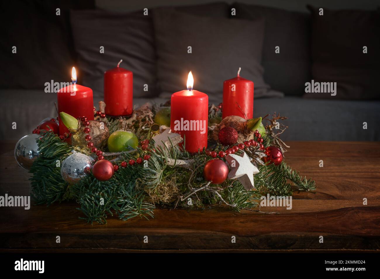 Adventskranz mit zwei brennenden roten Kerzen und Weihnachtsdekoration auf einem Holztisch vor der Couch, festliches Heimdekor für den zweiten Sonntag, Stockfoto