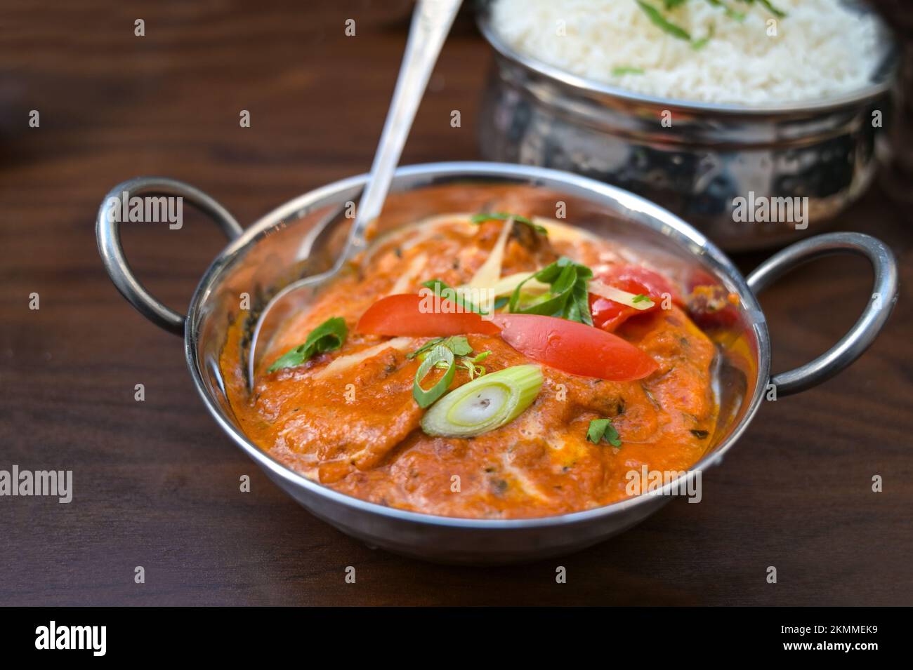 Indisches Currygericht mit Tomaten und Lauch in einer silbernen Schüssel serviert mit Reis auf einem dunkelbraunen Holztisch, Kopierbereich, ausgewählter Fokus, enge Tiefe des Torfes Stockfoto