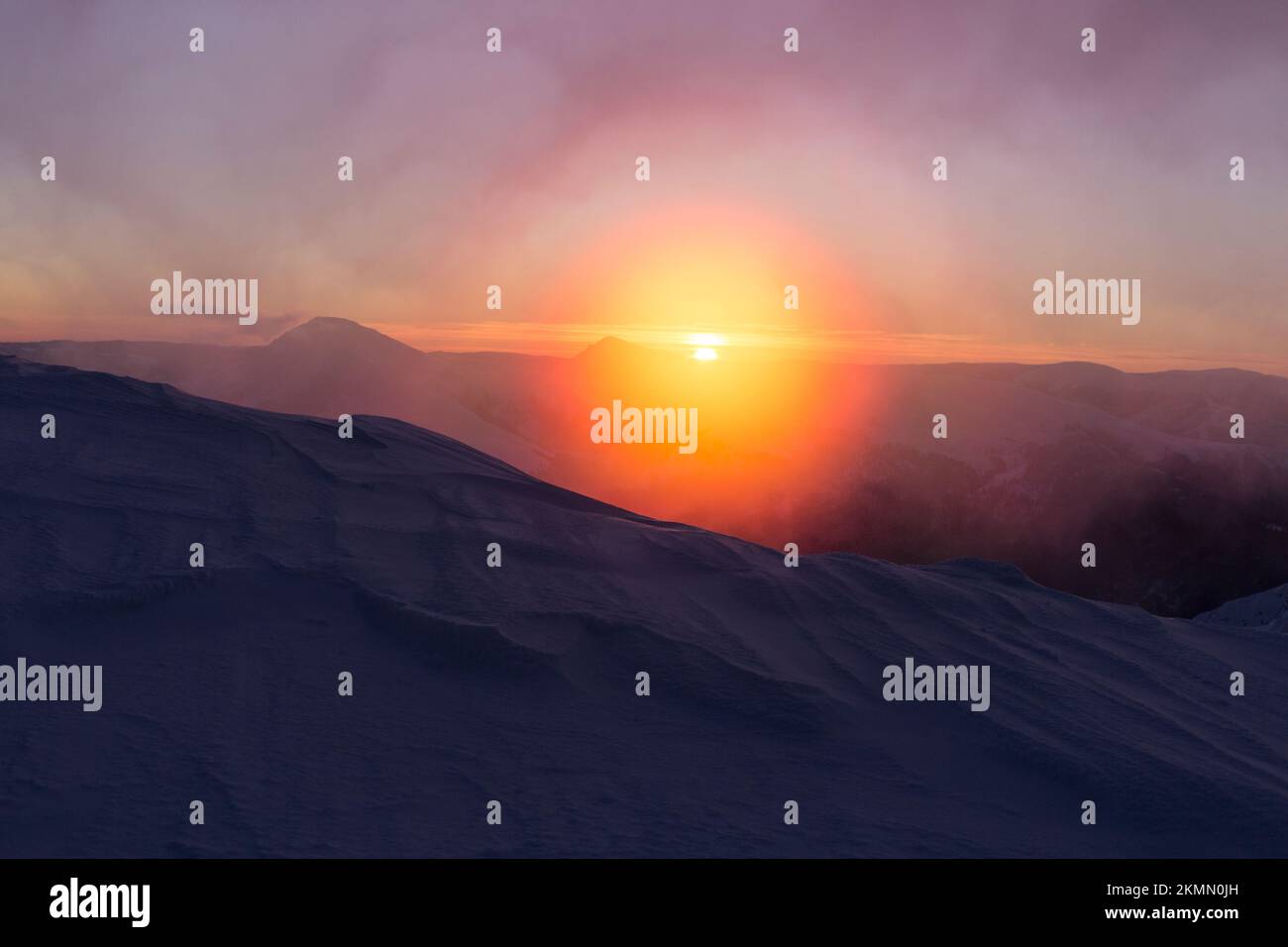 Leuchtend orangefarbener Sonnenaufgang der Sonnenscheibe in den schneebedeckten Bergen. Marmarosy, die Karpaten-Gebirgskette Stockfoto