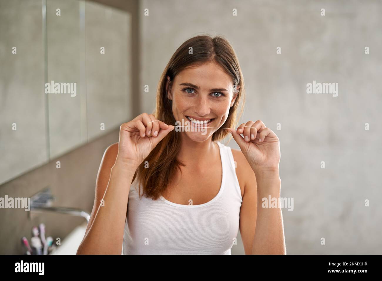 Ich werde eine Million Dollar Lächeln. Porträt einer jungen Frau, die im Bad Zahnseide benutzt. Stockfoto