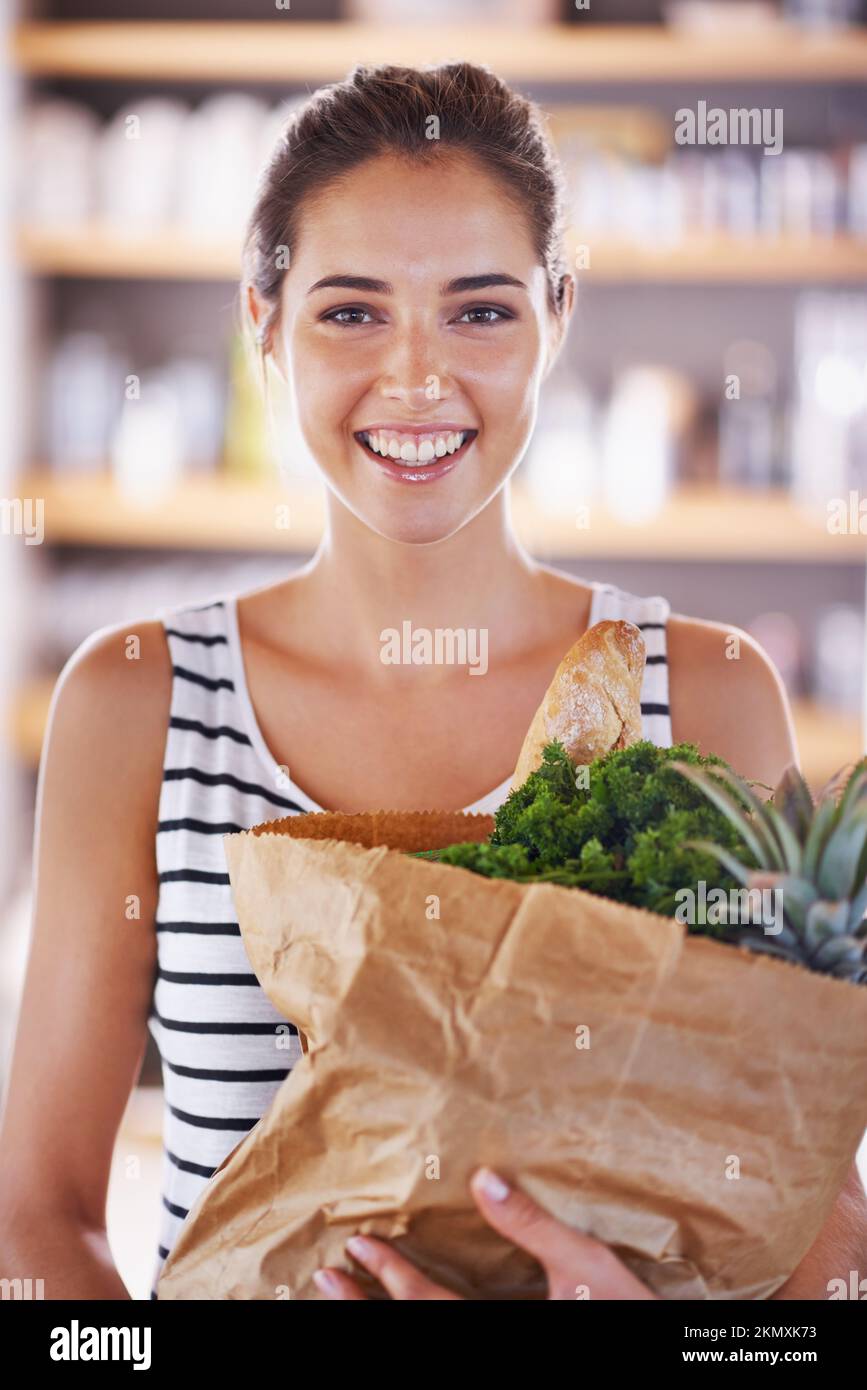 Ich fange mit meiner neuen Diät an. Eine attraktive Frau, die eine Tüte Lebensmittel in der Küche hält. Stockfoto