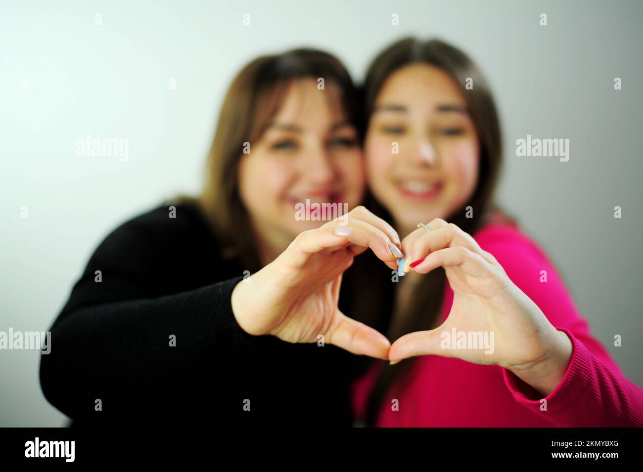 Mom und Tochter zeigen Herz aus den Händen, sie schauen in den Rahmen, berühren ihre Finger, Familienwarmliebe Stockfoto