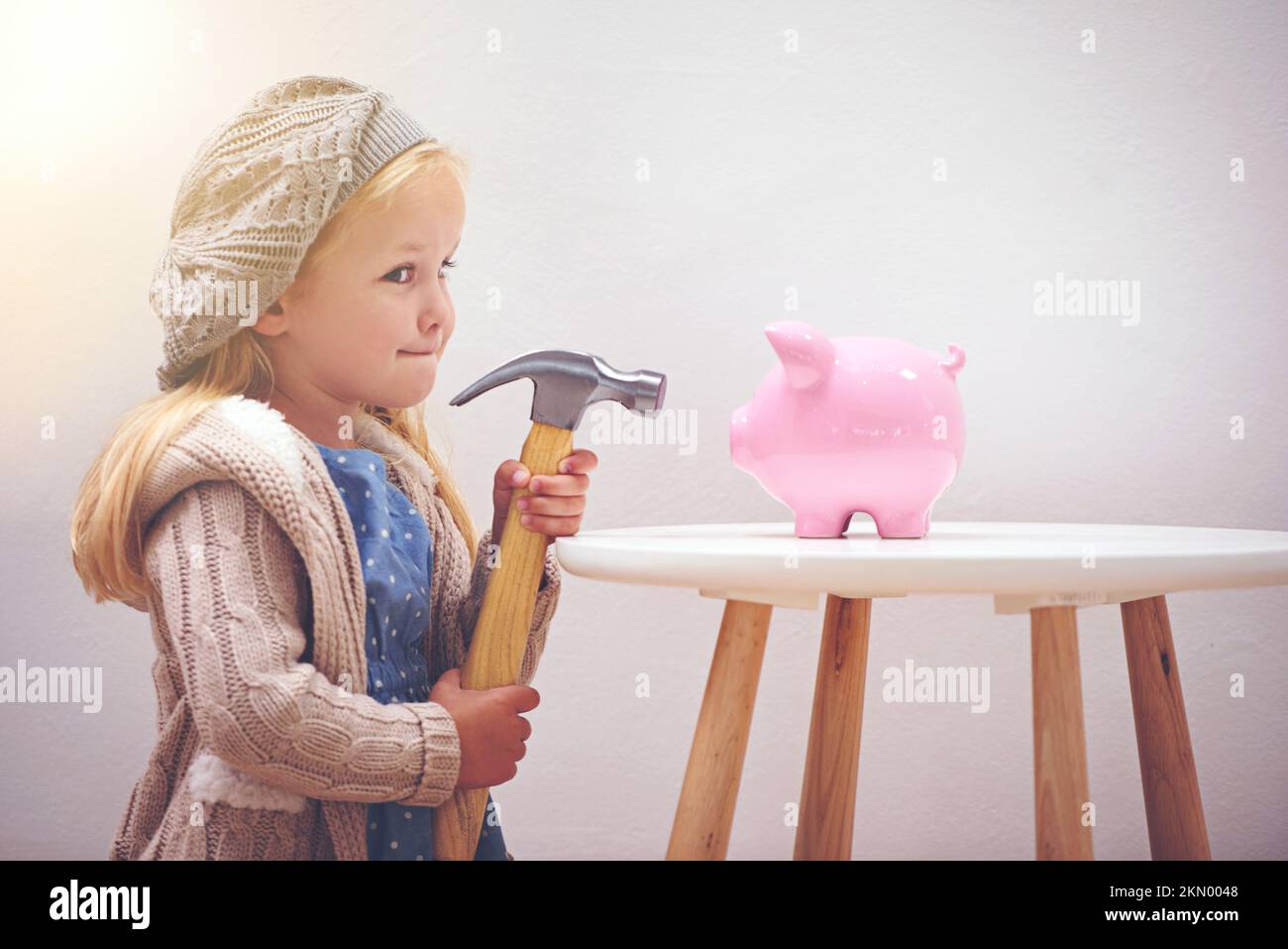 Verlockend, nicht wahr? Ein kleines Mädchen, das mit einem Hammer neben ihrem Sparschwein steht. Stockfoto