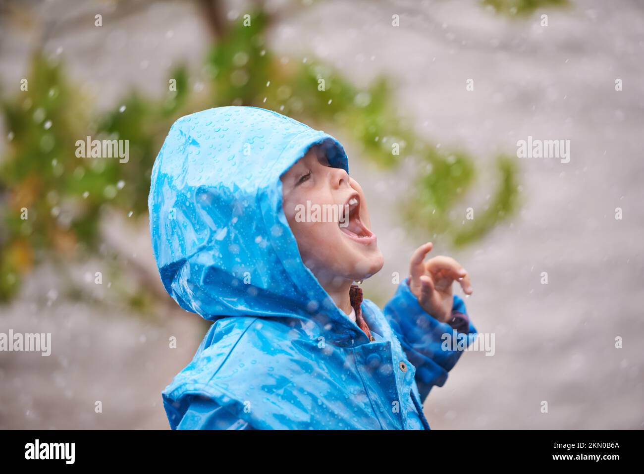 Schmecke den Regen. Ein kleiner Junge, der draußen im Regen spielt. Stockfoto