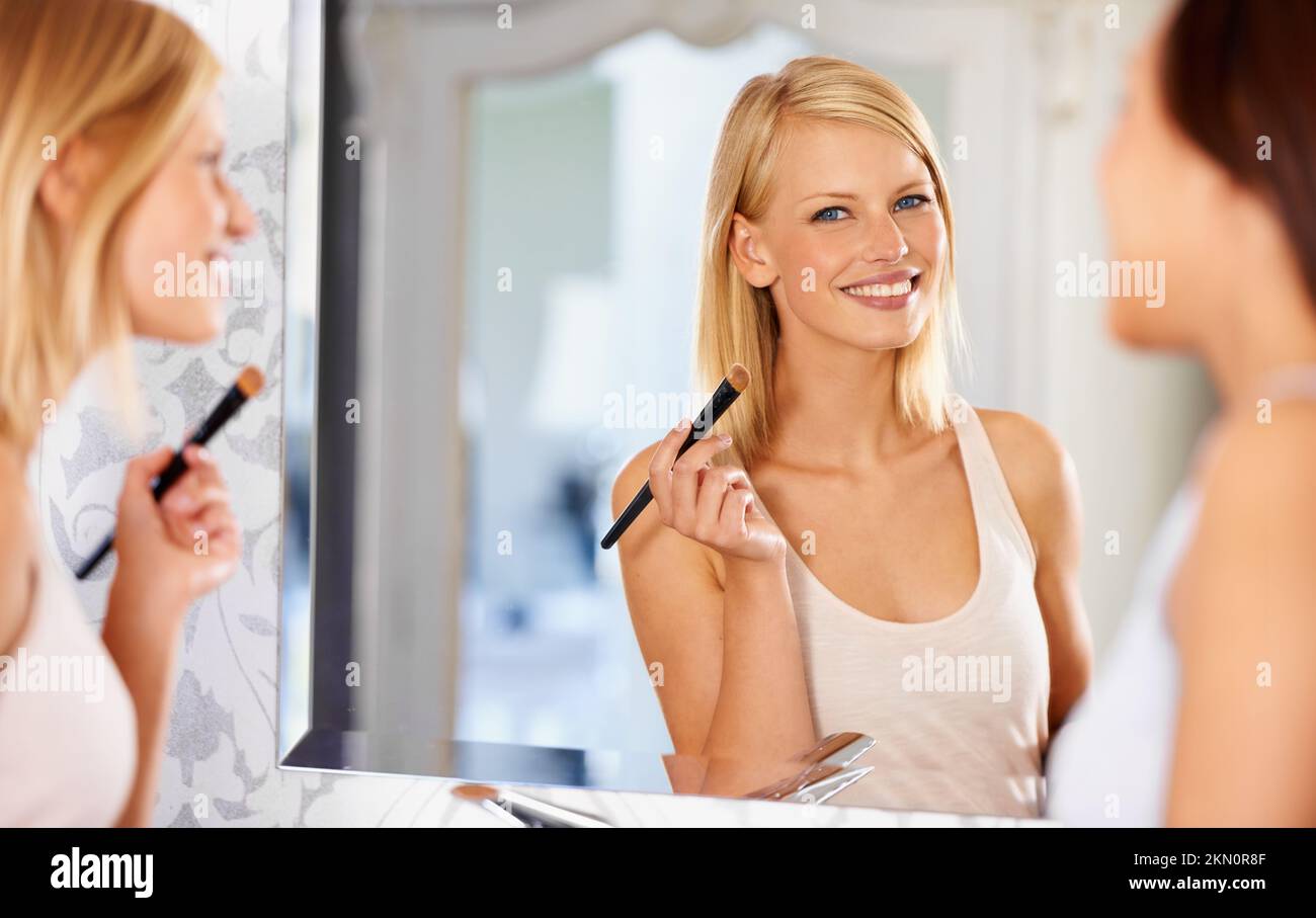 Du siehst wirklich umwerfend aus. Eine junge Frau schminkt sich vor dem Spiegel, während ihr Freund daneben steht. Stockfoto