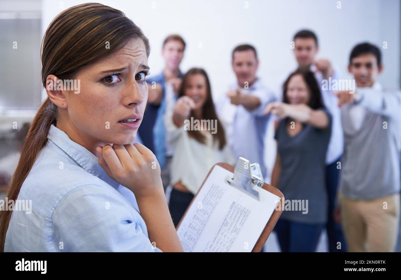 Ich glaube nicht, dass es gut läuft. Eine ängstliche junge Frau, die den Anschuldigungsfingern ihrer Kollegen gegenübersteht. Stockfoto
