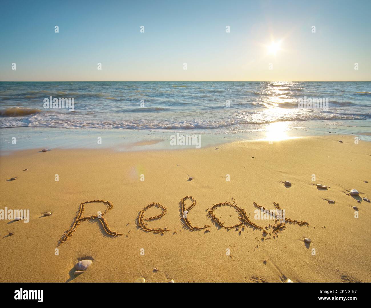 Wort entspannen handgeschrieben am Sandstrand bei Sonnenuntergang. Natur und konzeptuelle Szene. Stockfoto