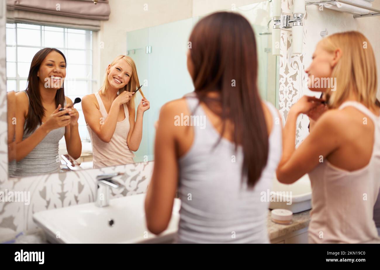 Etwas, das wir beide lieben... zwei junge Frauen, die Make-up auftragen und ihre Haare vor dem Spiegel stylen. Stockfoto