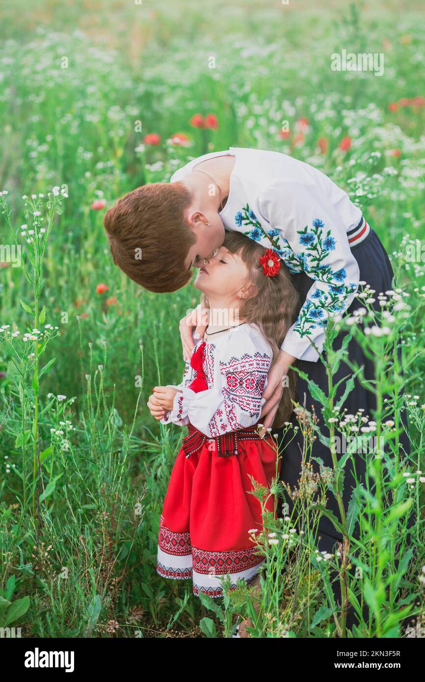 Mom in ukrainischem Nationalkleid küsst ihre Tochter in Blumen Stockfoto