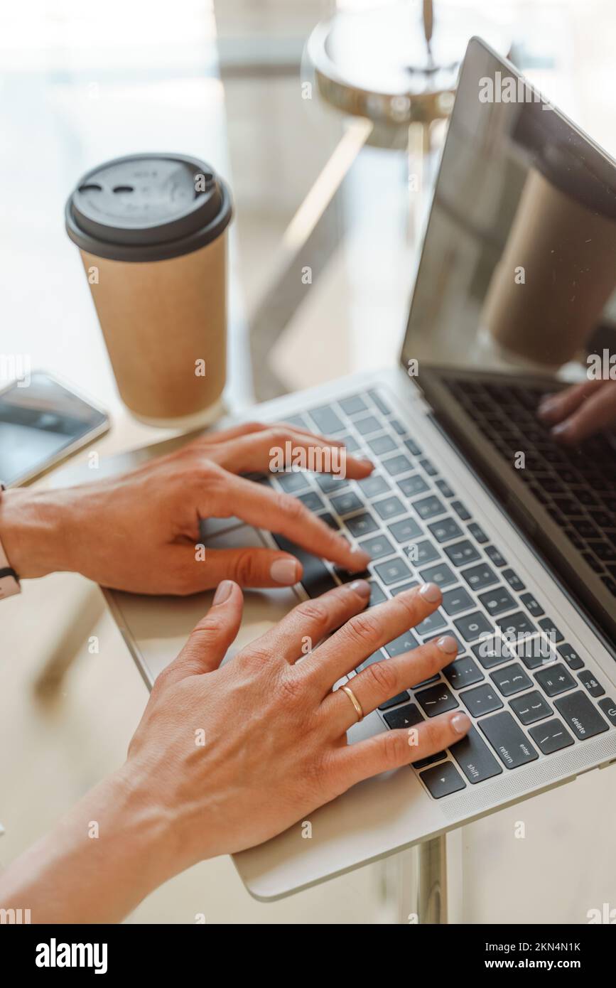 Hände, die auf einer Computertastatur über einem weißen Bürotisch mit einer Tasse Kaffee und Zubehör tippen, Draufsicht. Stockfoto