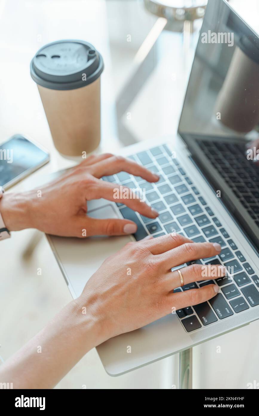 Hände, die auf einer Computertastatur über einem weißen Bürotisch mit einer Tasse Kaffee und Zubehör tippen, Draufsicht. Stockfoto