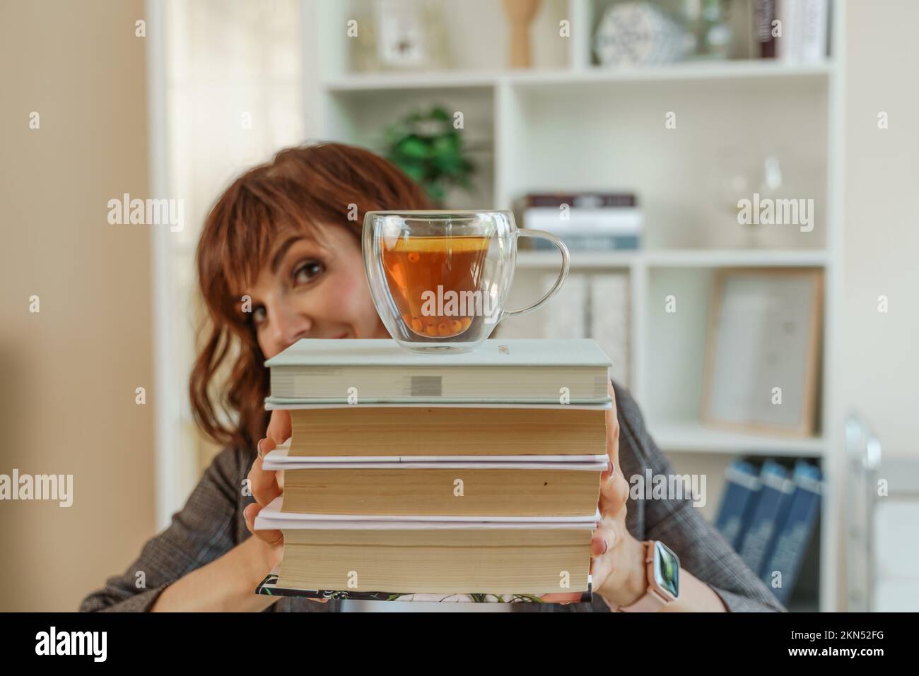 Die Frau bucht eine Tasse Tee. Die Schülerin hält die Bücher vor sich und verdeckt ihr Gesicht. Auf einem Stapel Bücher befindet sich eine durchsichtige Tasse Tee Stockfoto