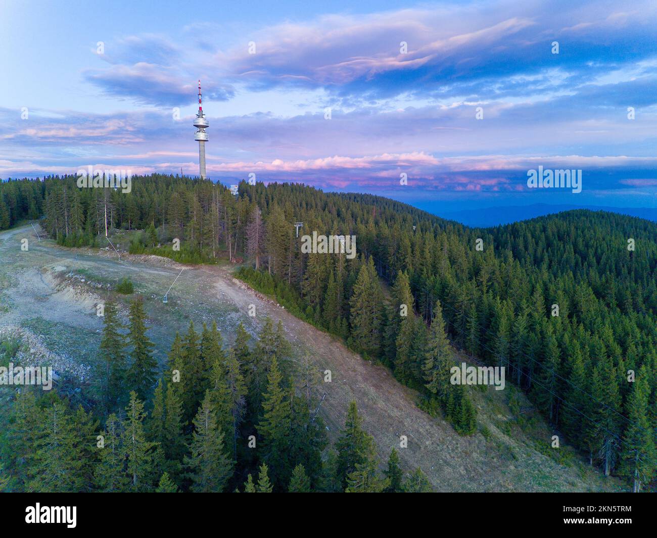 Hoher Telekommunikationsturm Snezhanka auf einem Berg im Tal der Rhodope Berge mit Nebel, Wald, Sonnenstrahlen und sonnigen Wolken Stockfoto