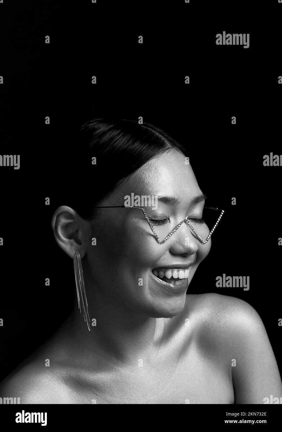 Schwarzweißfoto. Ein asiatisches Mädchen mit schwarzem Hintergrund im Studio. Gold. Gelächter. Stockfoto