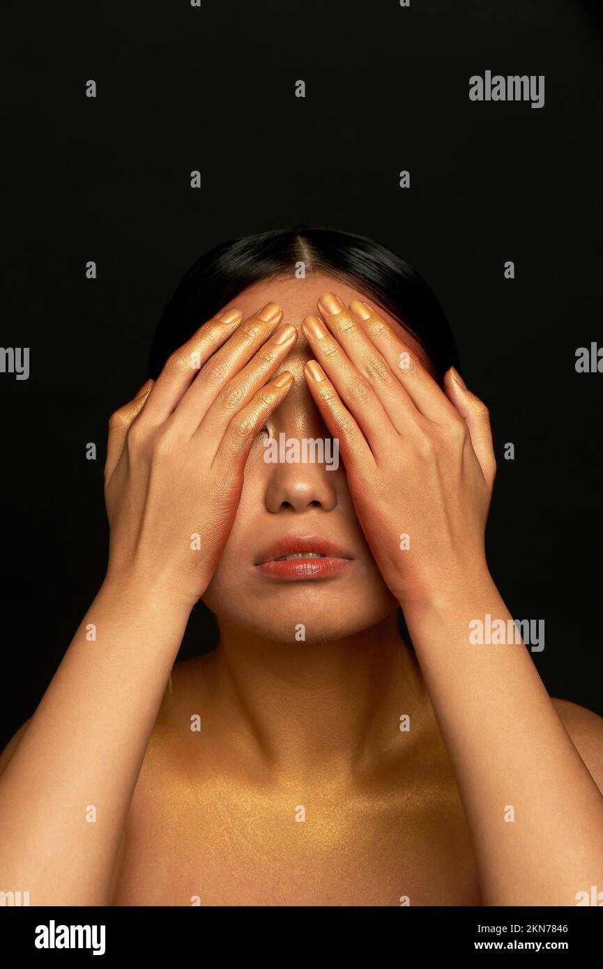 Ich sehe das Böse nicht. Ein asiatisches Mädchen mit schwarzem Hintergrund in einem Fotostudio. Gold. Stockfoto