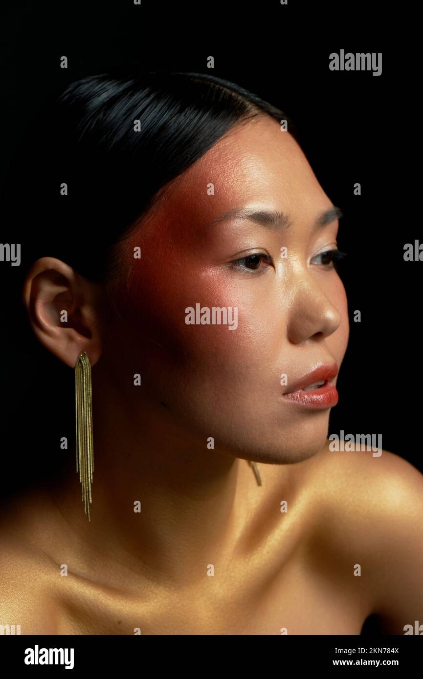 Ein asiatisches Mädchen mit goldener Haut sieht im Profil aus. Lange goldene Ohrringe. Schönheitssalon. Stockfoto
