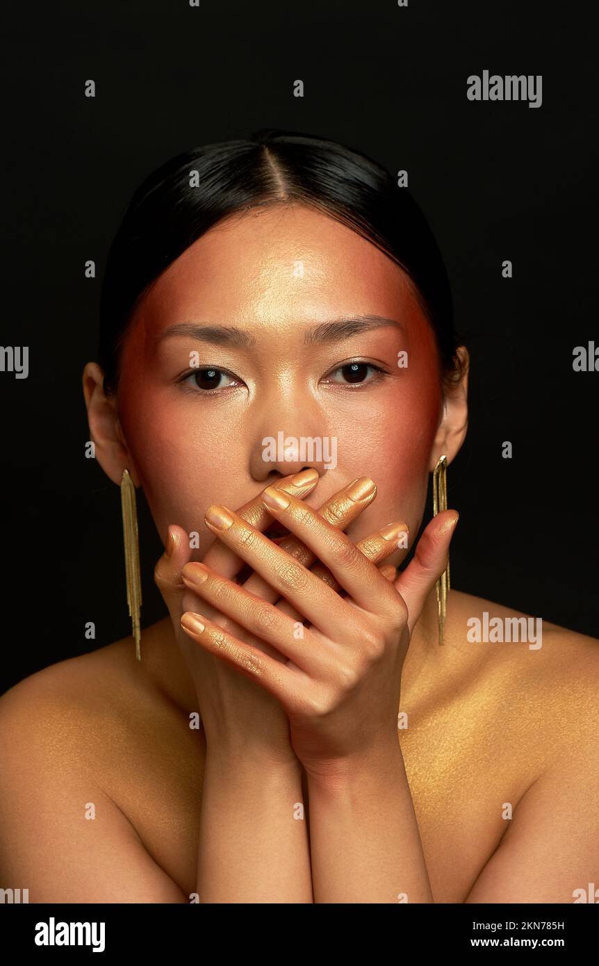 Ich rede nicht vom Bösen. Ein asiatisches Mädchen mit schwarzem Hintergrund im Studio. Gold. Stockfoto