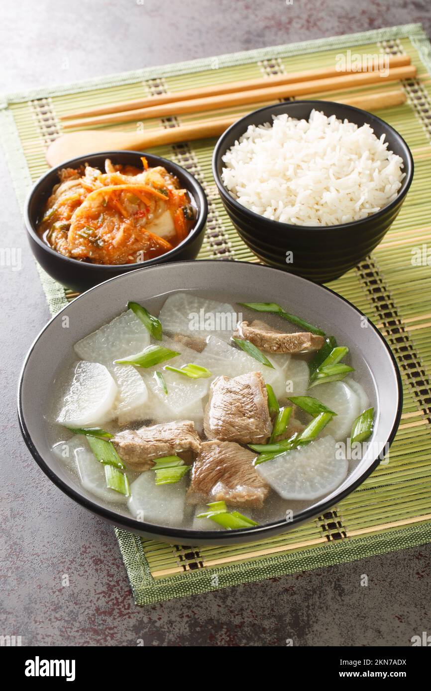 Koreanische Rindersuppe Sogogi Muguk serviert mit Reis und Kimchi Nahaufnahme auf der Matte auf dem Tisch. Vertikal Stockfoto