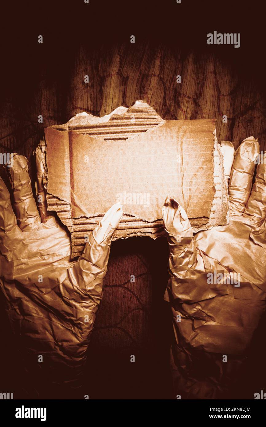 Nahaufnahme der Hände der Mumie, die Pappe hält. Getöntes Bild von Halloween Kreatur mit dickem Papier gegen Holzwand. Stockfoto