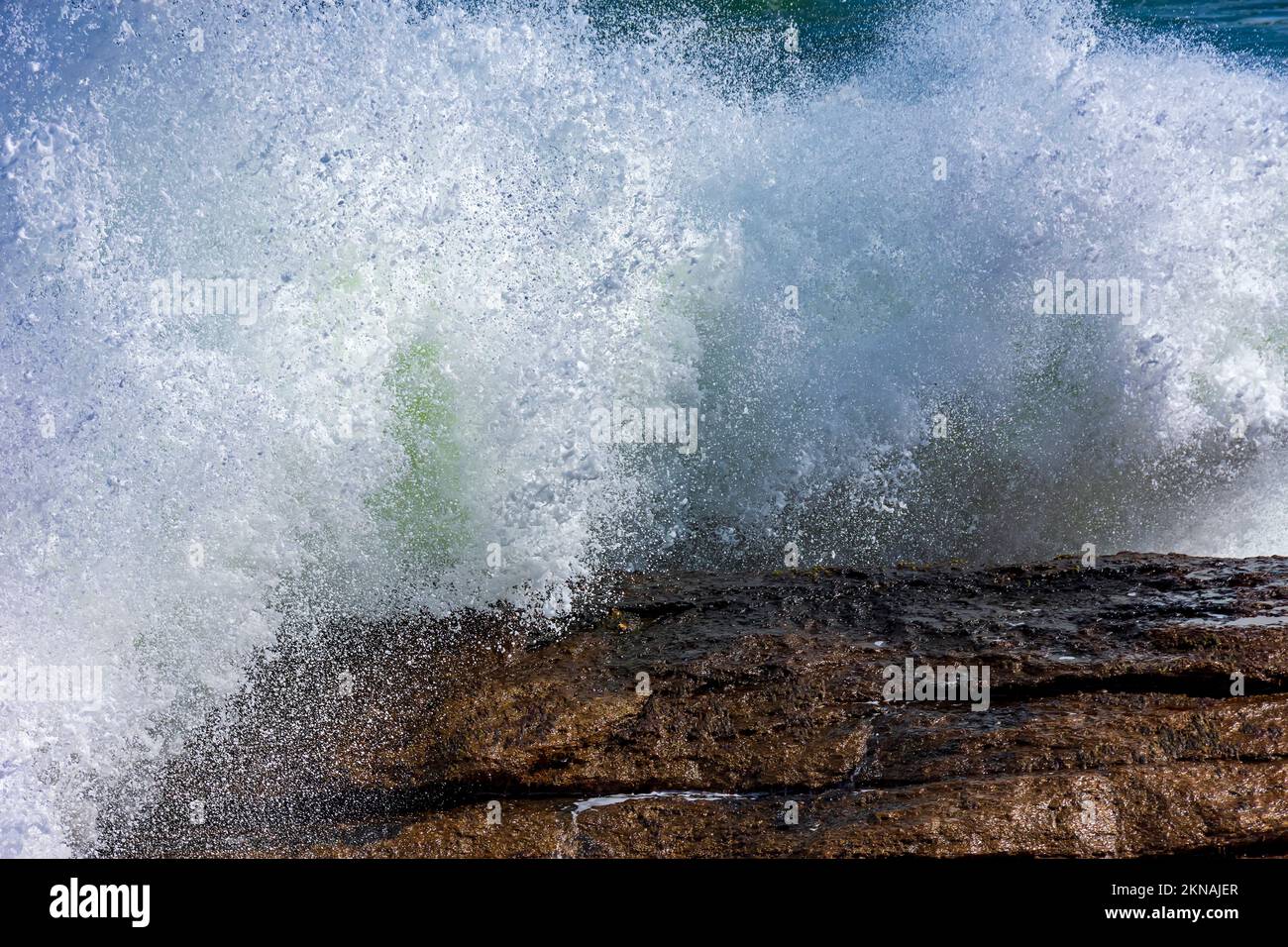 Starke Welle, die gegen die Felsen stürzt, mit Meerwasser und Schaum, der in die Luft spritzt Stockfoto