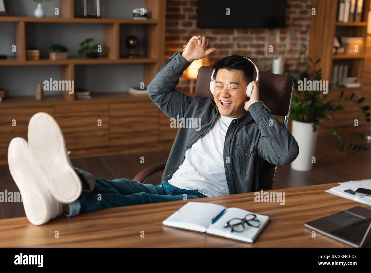 Ein gereifter Japaner in lässigen und kabellosen Kopfhörern hört Musik, entspannt euch, genießt die Audio-App am Tisch Stockfoto