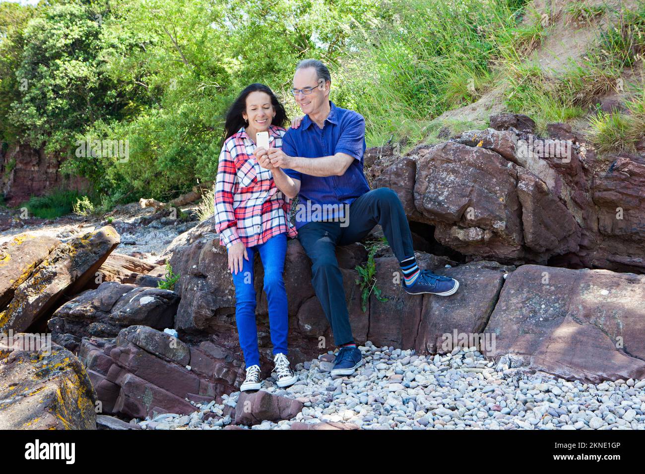 Mann und Frau, die sich an der Küste gegen Felsen ausruhen Stockfoto