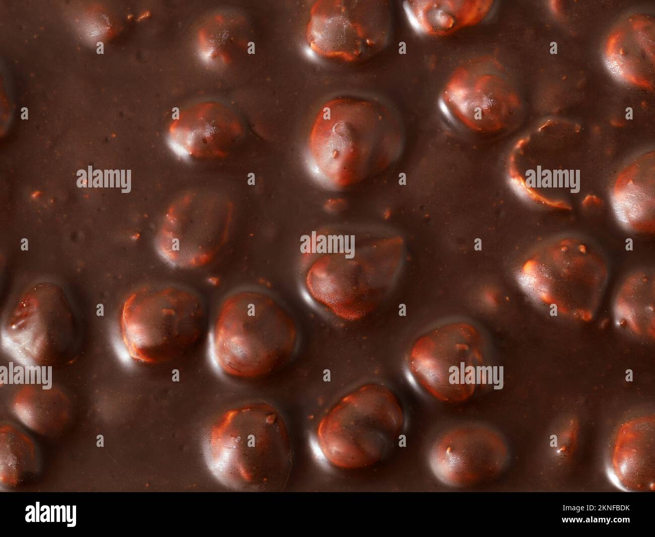 Leckere dunkle Schokolade mit Haselnüssen als Hintergrund, Blick von oben auf die in dunkler Schokolade geschmolzenen Haselnüsse Stockfoto