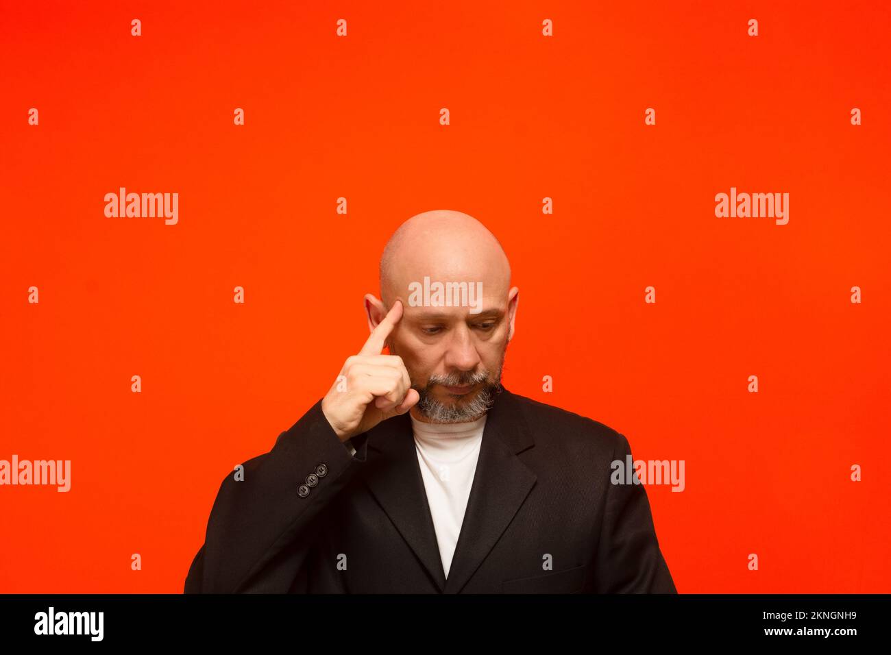 Geschäftsmann, trägt eine schwarze Anzugjacke, schlau und aufmerksam. Isoliert auf orangefarbenem Hintergrund. Stockfoto