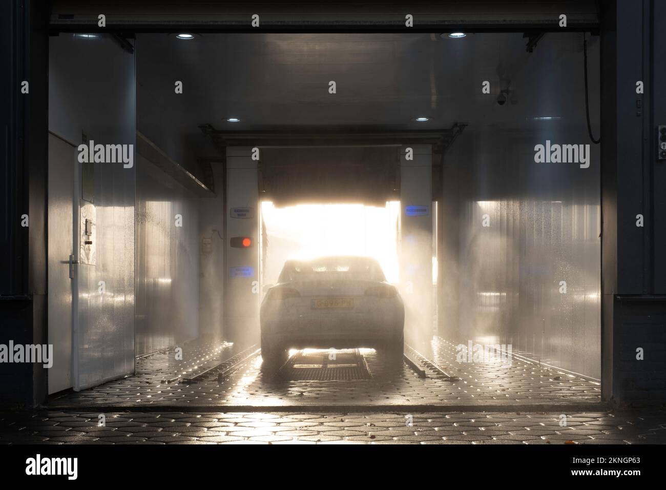Das Fahrzeug wird in einer überdachten automatischen Waschanlage mit Waschprogramm gewaschen. Die Bürsten drehen sich über und neben dem Fahrzeug. Sonnenlichteffekt. Autowaschanlage Stockfoto