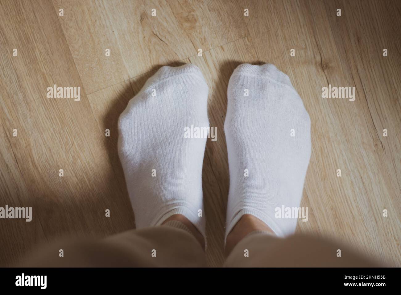 Weiße Socken auf dem Boden. Damenschuhe. Warmes Bekleidungskonzept. Bequeme Baumwollkleidung. Familiäre Hintergründe. Weiße Socken auf Mädchenfüßen. Stockfoto