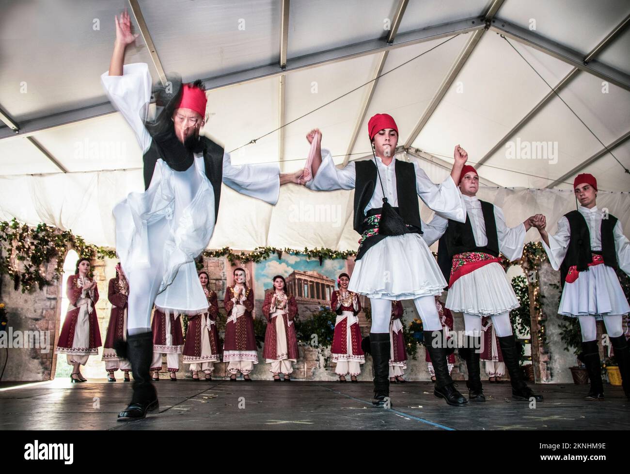 09.-21-2019. Tulsa USA: Kostümierte griechische Tänzer in einem dekorierten Zelt mit dramatischem Kick auf dem Greek Festival in Tulsa, während Tänzerinnen klatschen Stockfoto