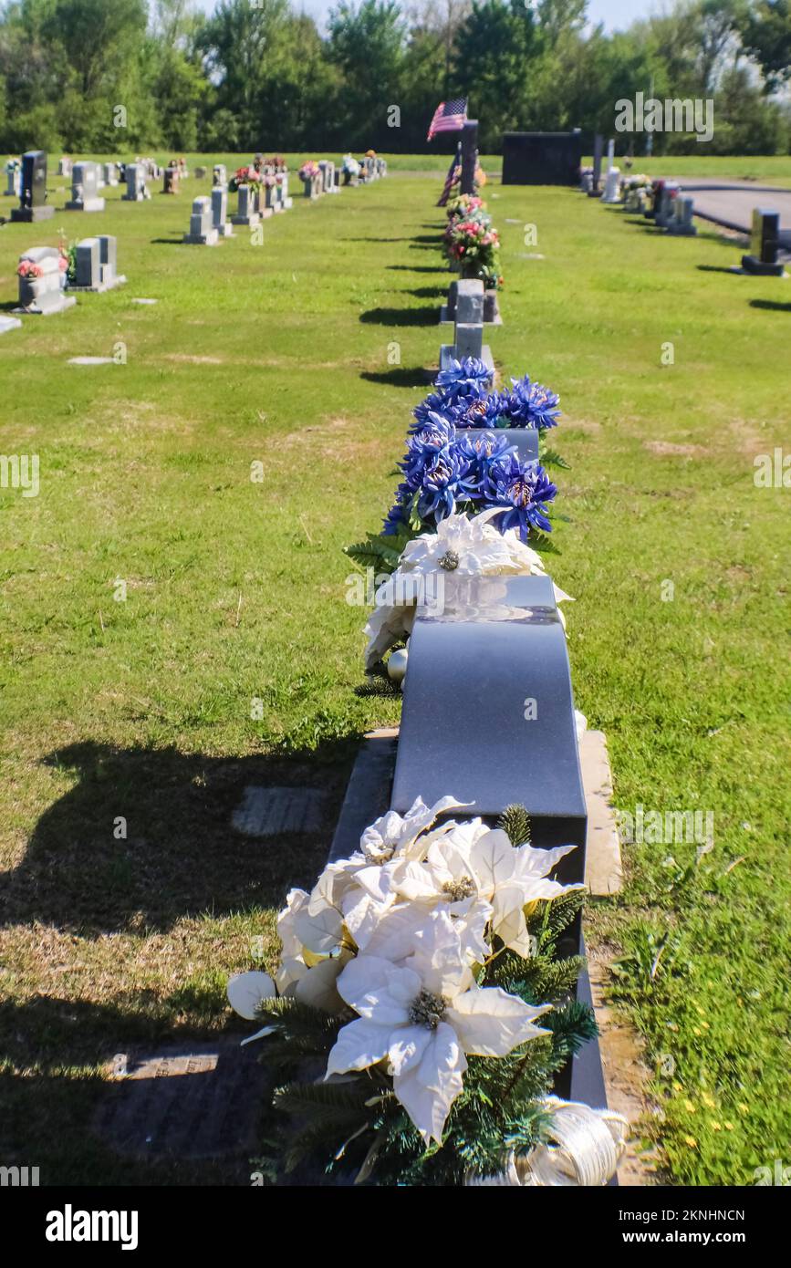 Blumen schmücken die Grabsteine für den Memorial Day auf dem Friedhof im Herzen der USA mit der US-Flagge im Hintergrund - selektive Füchse Stockfoto