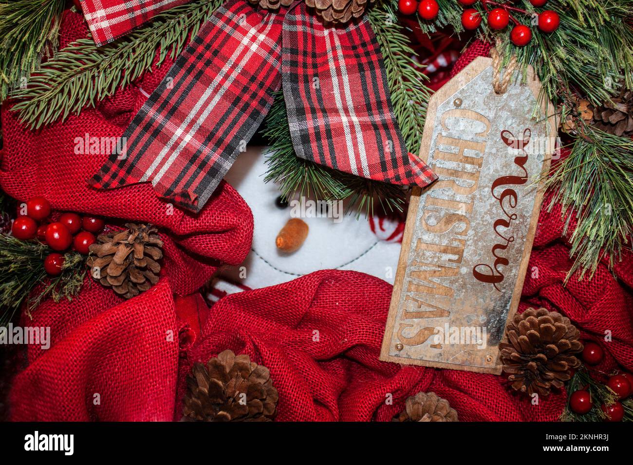 Guck-Guck-Weihnachtsmann sieht sich durch die Weihnachtsdekorationen mit rotem Burlap und Pinienzapfen und Beeren mit dem Anhänger „Merry Christmas“ an Stockfoto