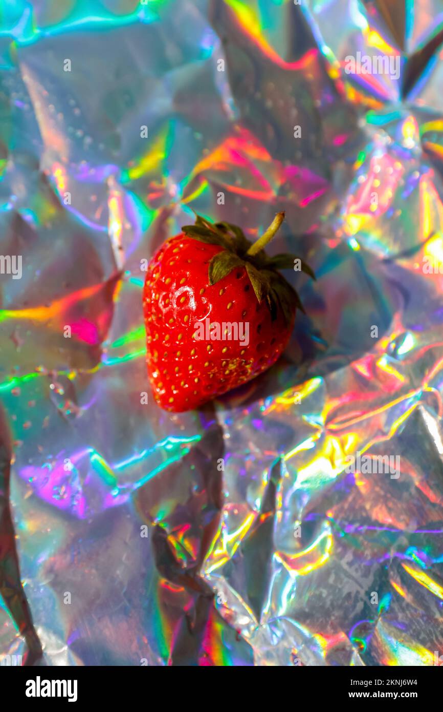 Unschärfe-Nahaufnahme eine reife rote Erdbeere auf modernem Hologramm-Hintergrund. Obst und Beeren. Erntegutkonzept. Organisch. Trendige Gradienten. Glänzende Folie Stockfoto