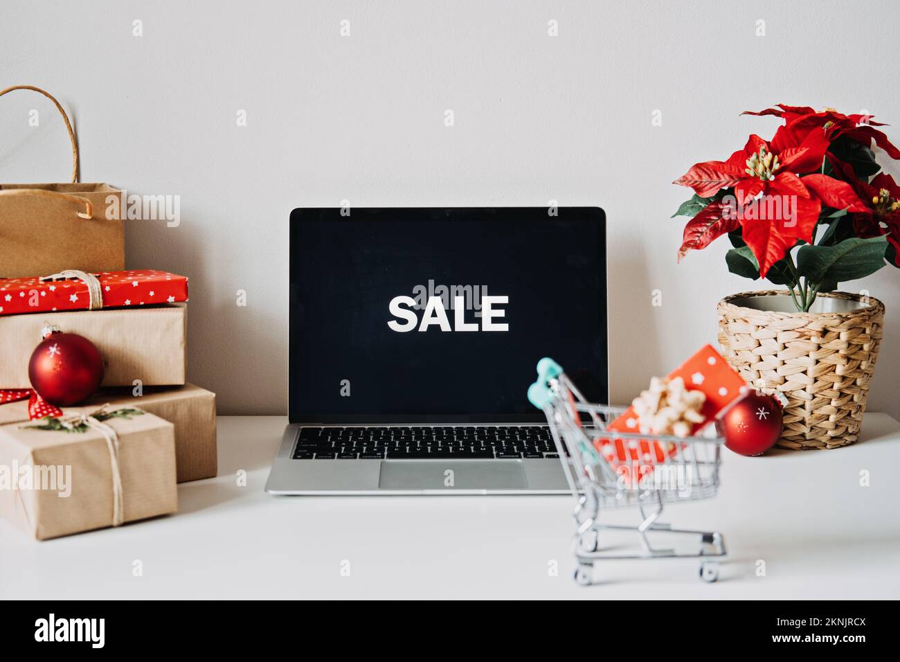 Offener Laptop mit Word Sale auf Display, Poinsettias Weihnachtsblume und Geschenkboxen auf weißem Tisch. Weihnachten online-Shopping, Winter Stockfoto