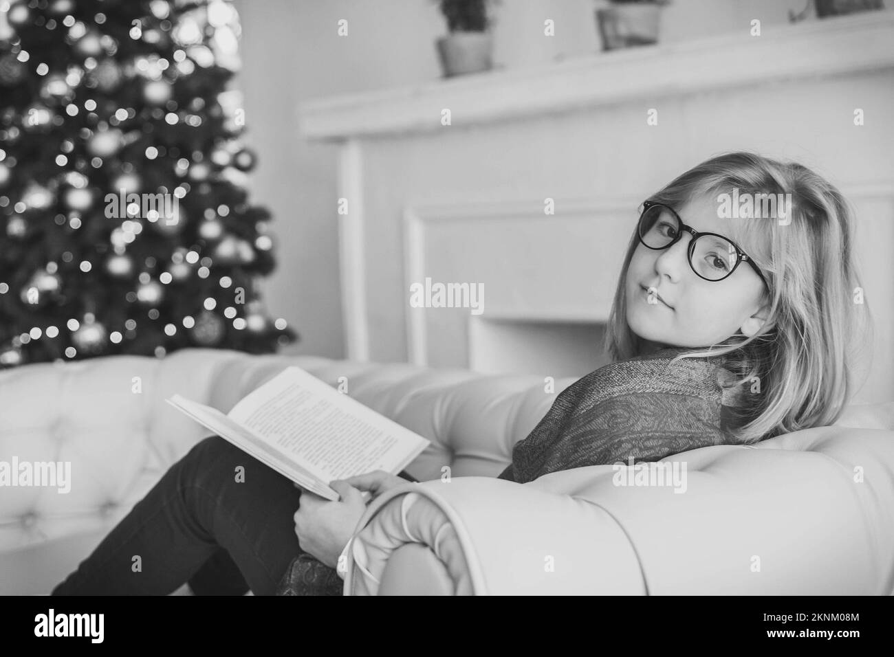 Hübsches Mädchen, das ein Buch auf dem Sofa neben dem weihnachtsbaum liest Stockfoto