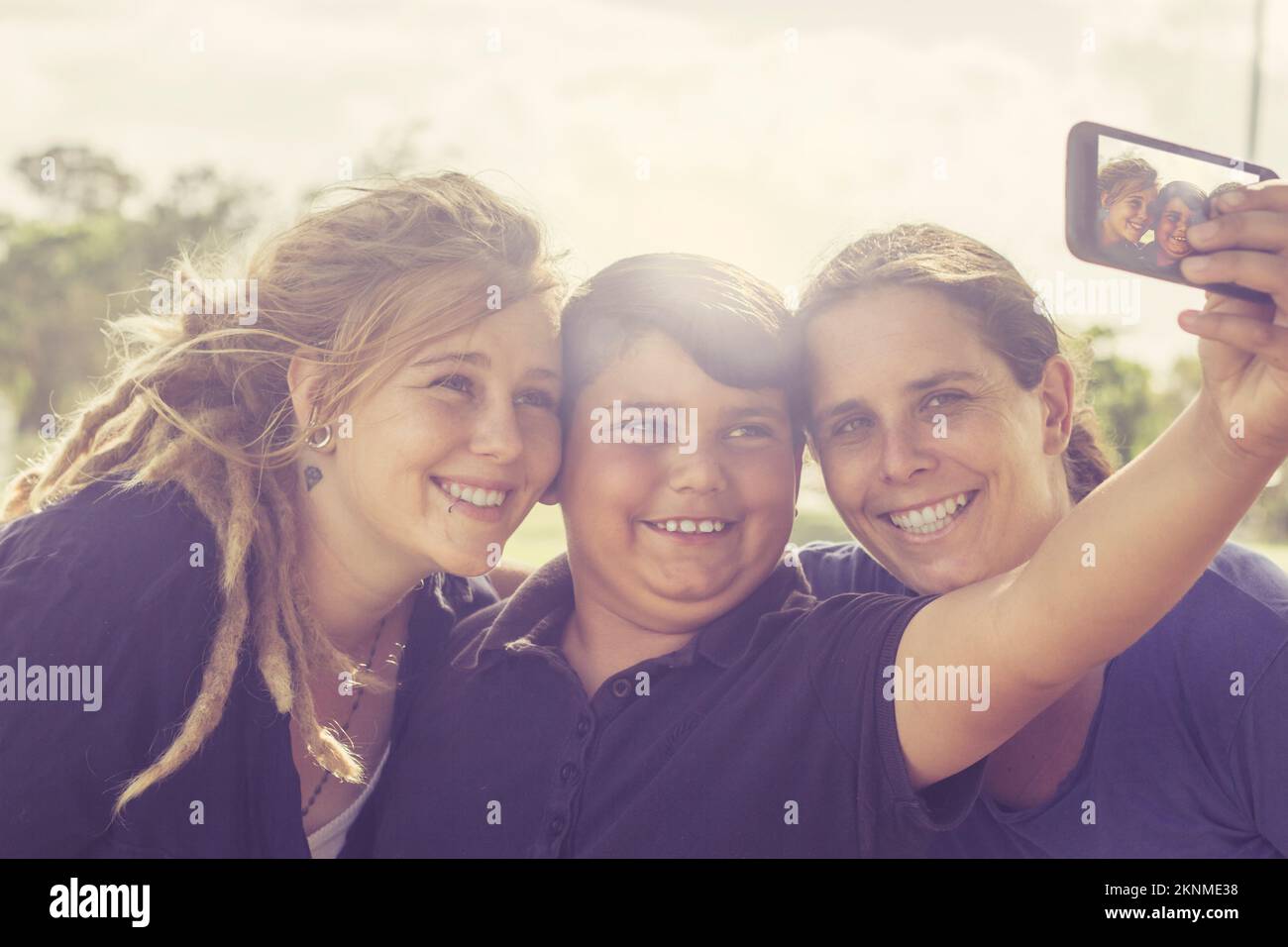 Fröhliche australische multikulturelle Familie aus drei Personen, die im Freien stehen und Selfie mit dem Smartphone machen. Familien mit technischen Geräten Stockfoto