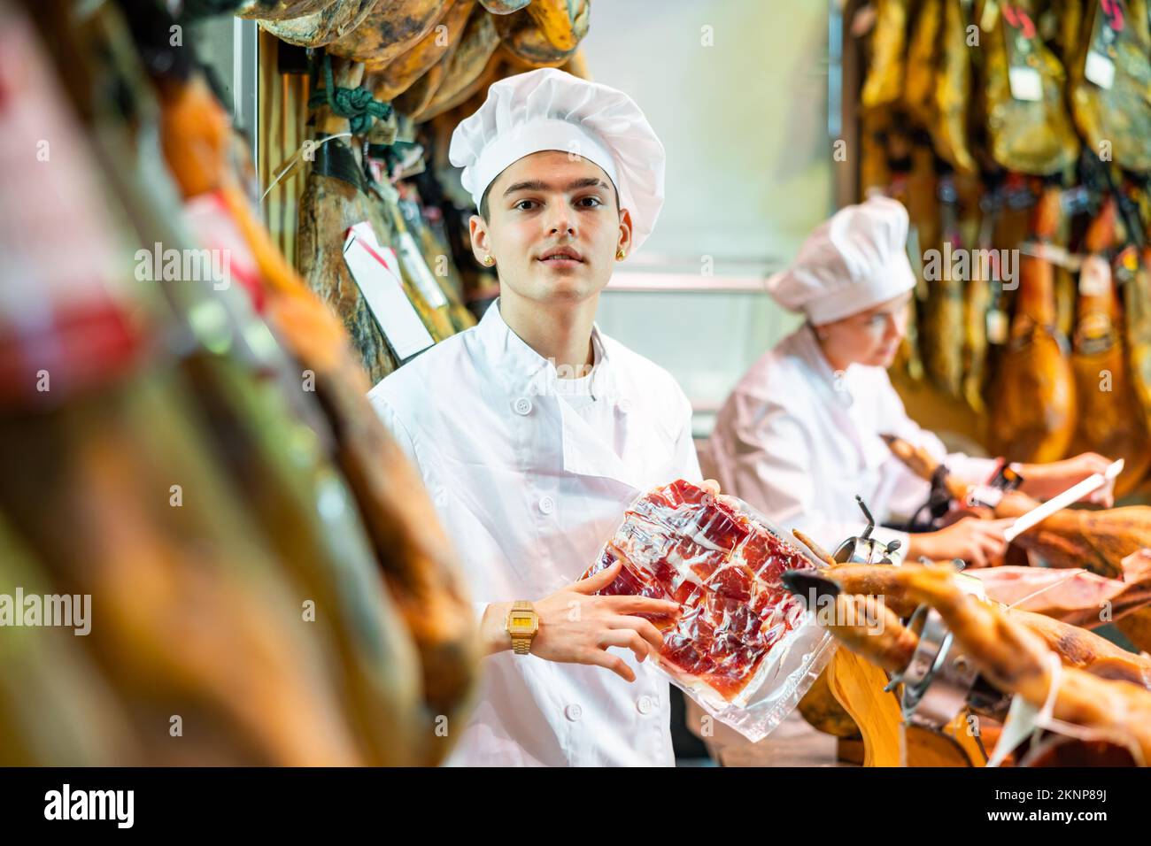 Junger Vertreter des Metzgerladens in weißer Uniform, der iberischen Pyjon in Scheiben anbietet Stockfoto