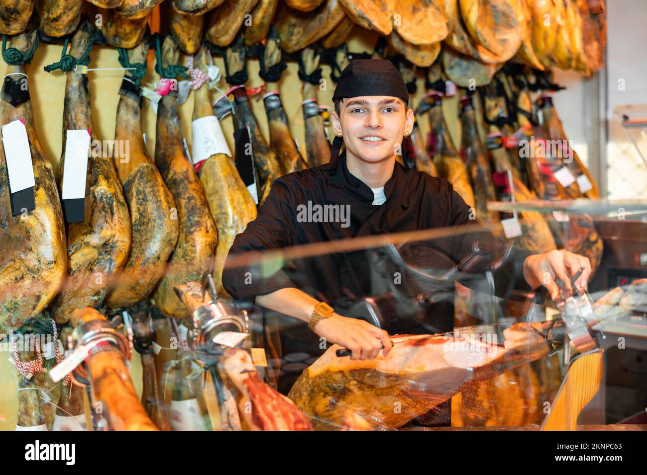 Junger Verkäufer in schwarzer Uniform, der an der Theke in der Metzgerei einen Pyjon schneidet Stockfoto