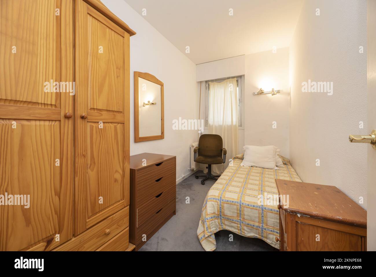 Ein schmales Schlafzimmer mit einem jugendlichen Bett und unpassenden Holzmöbeln und einem lackierten Kiefernschrank Stockfoto